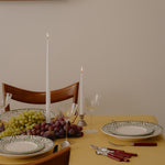 Dining table set with plates, glasses, and cutlery on a yellow tablecloth.