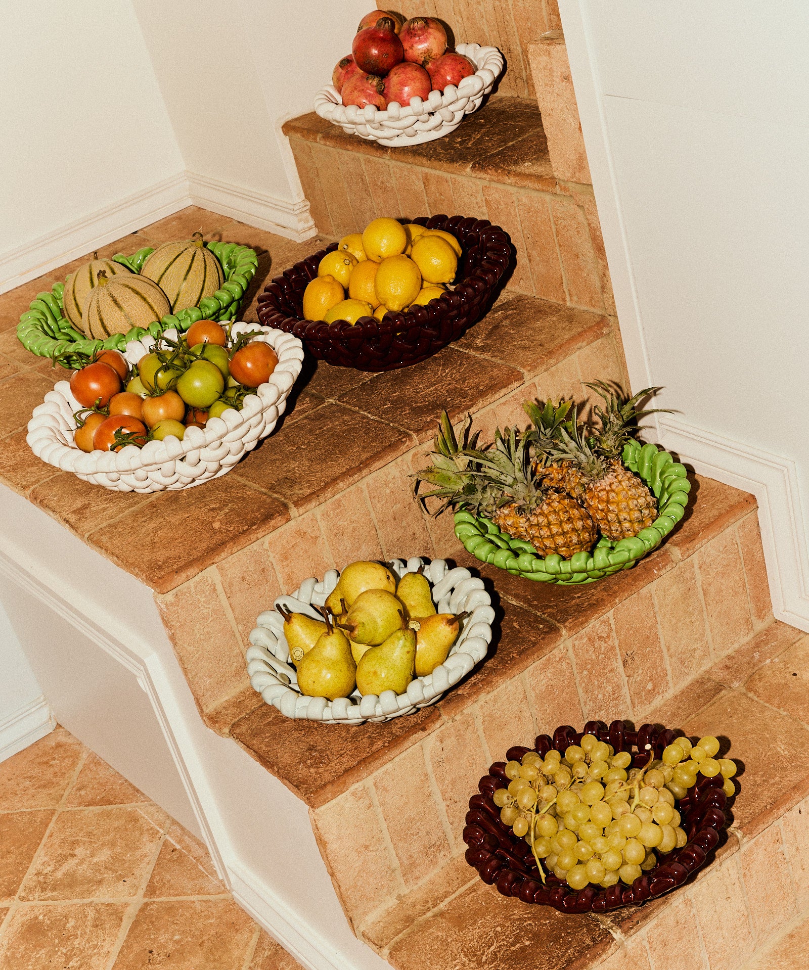 Fruit bowls on a staircase with various fruits including apples, oranges, pears, and grapes.