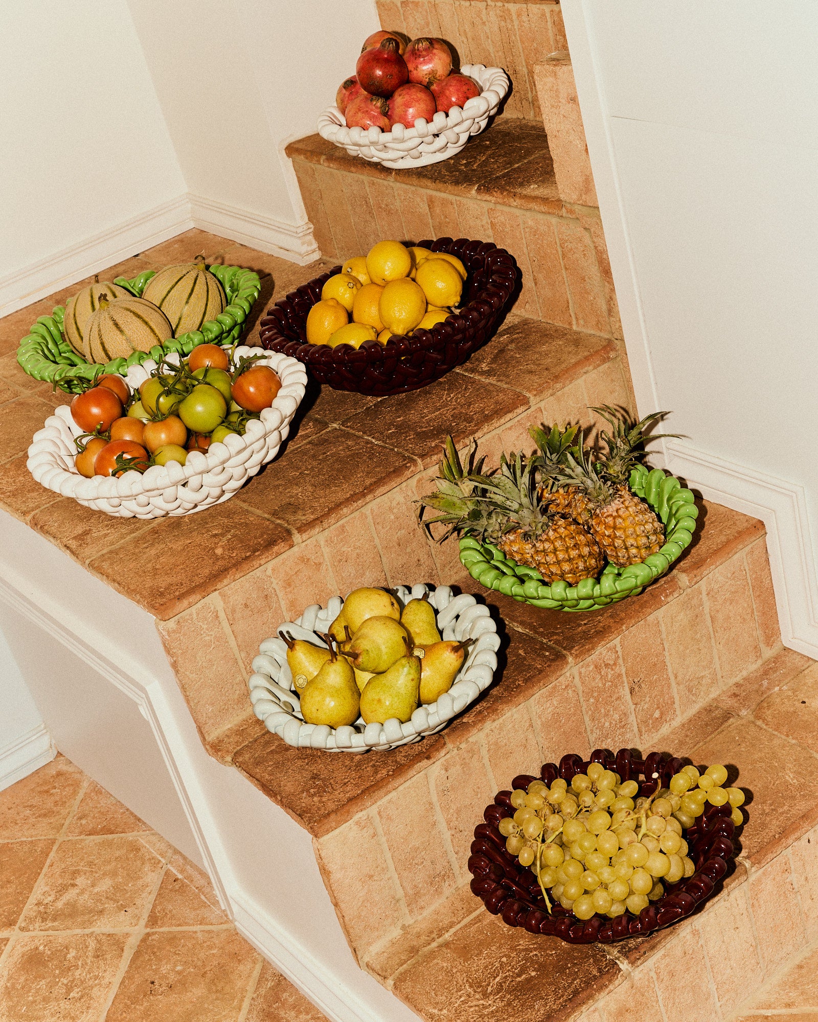 Fruit bowls on a staircase with various fruits including apples, oranges, pears, and grapes.