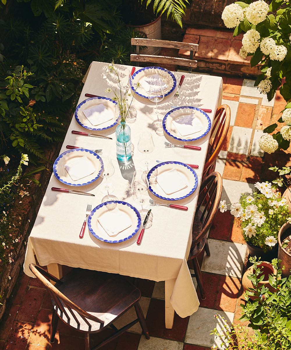 Dining table set for a meal outdoors with plates, cutlery, and glasses on a checkered patio.