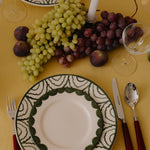 Dinner setting with a decorative plate, grapes, figs, and cutlery on a yellow tablecloth.