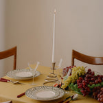 Dining table set with plates, glasses, candles, and grapes on a yellow tablecloth.