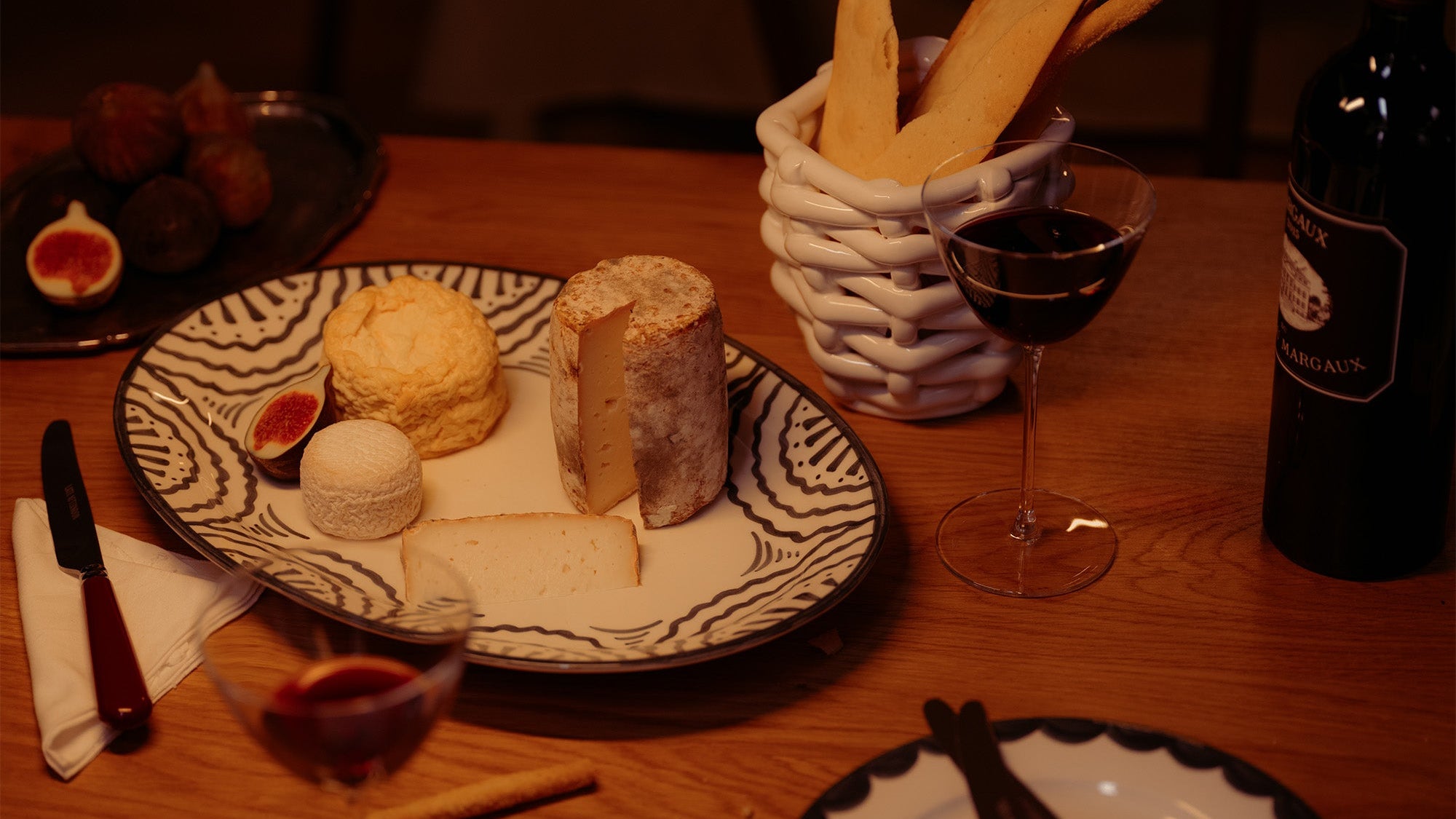 Table setting with cheese plate, wine glasses, and bread on a wooden table.