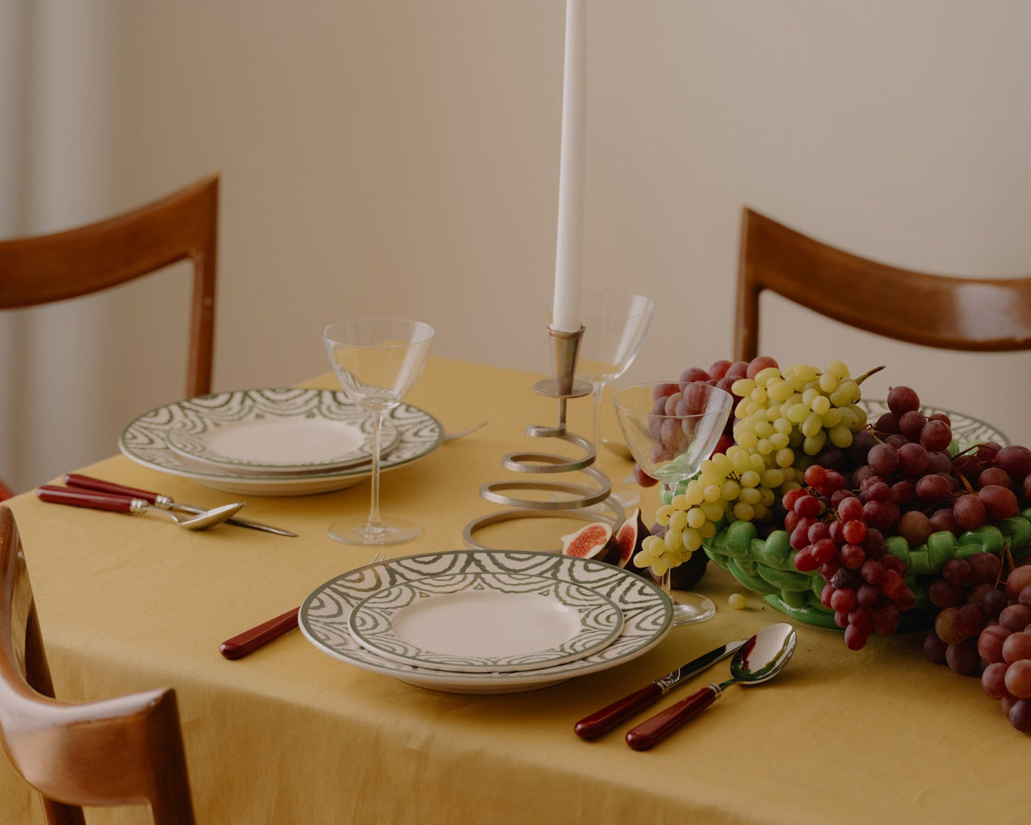 Dining table set with plates, glasses, and fruits on a yellow tablecloth.