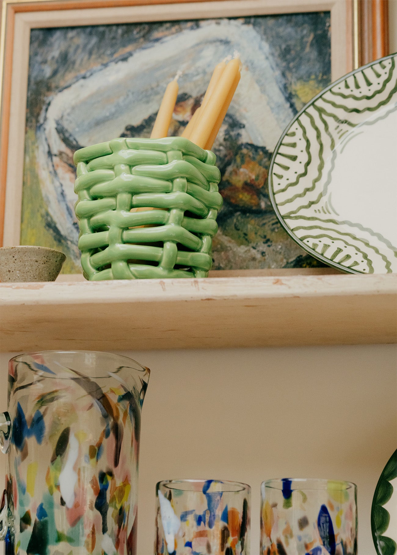 Decorative green basket with candles on a shelf with abstract art in the background