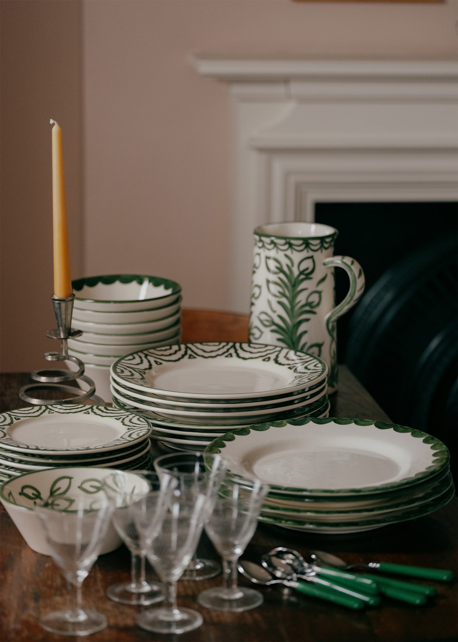 Dining table set with green and white patterned plates, cups, and glasses in front of a fireplace.