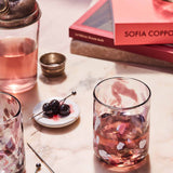 Pink cocktail in a glass with cherries on a marble surface.