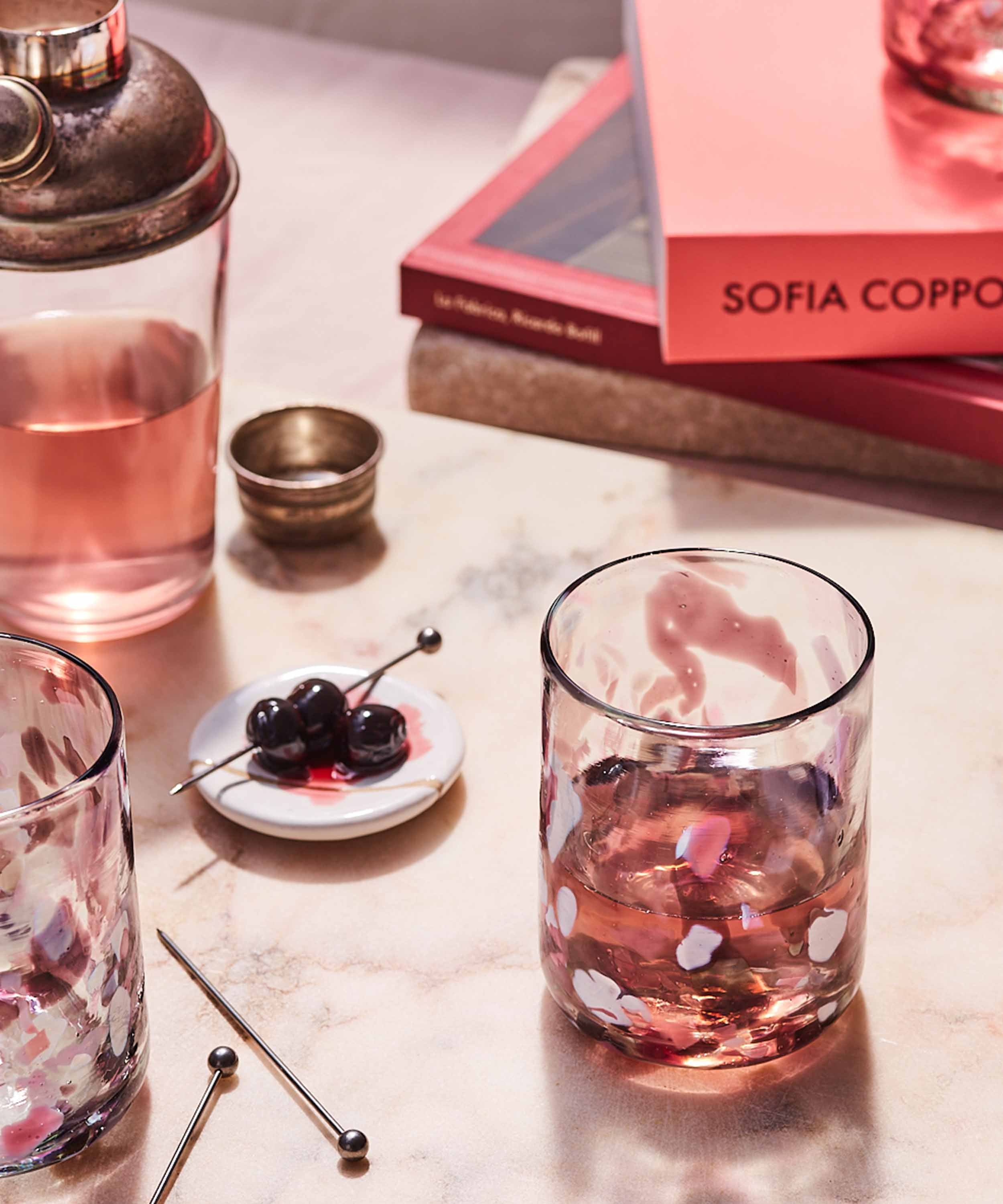 Pink cocktail in a glass with cherries on a marble surface.
