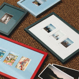 Four picture frames in red, dark teal, and light blue, arranged on a brown woven rug with sample photographs inside and beside them.