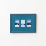 A rectangular Petrol Blue picture frame with three small printed photographs mounted side by side, shown hanging on a plain white wall.