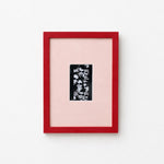 A framed art print featuring a black and white floral pattern on a light pink mat, enclosed in a vibrant red frame against a clean white background.