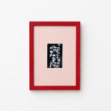A framed art print featuring a black and white floral pattern on a light pink mat, enclosed in a vibrant red frame against a clean white background.