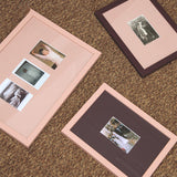 Three rectangular picture frames with pale pink borders and burgundy inner mats are arranged on a brown carpeted floor. 