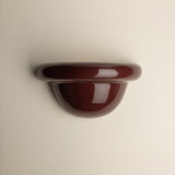 A glossy, dark reddish-brown wall-mounted shelf or hook with a rounded, semi-circular profile, shown against a plain off-white background.