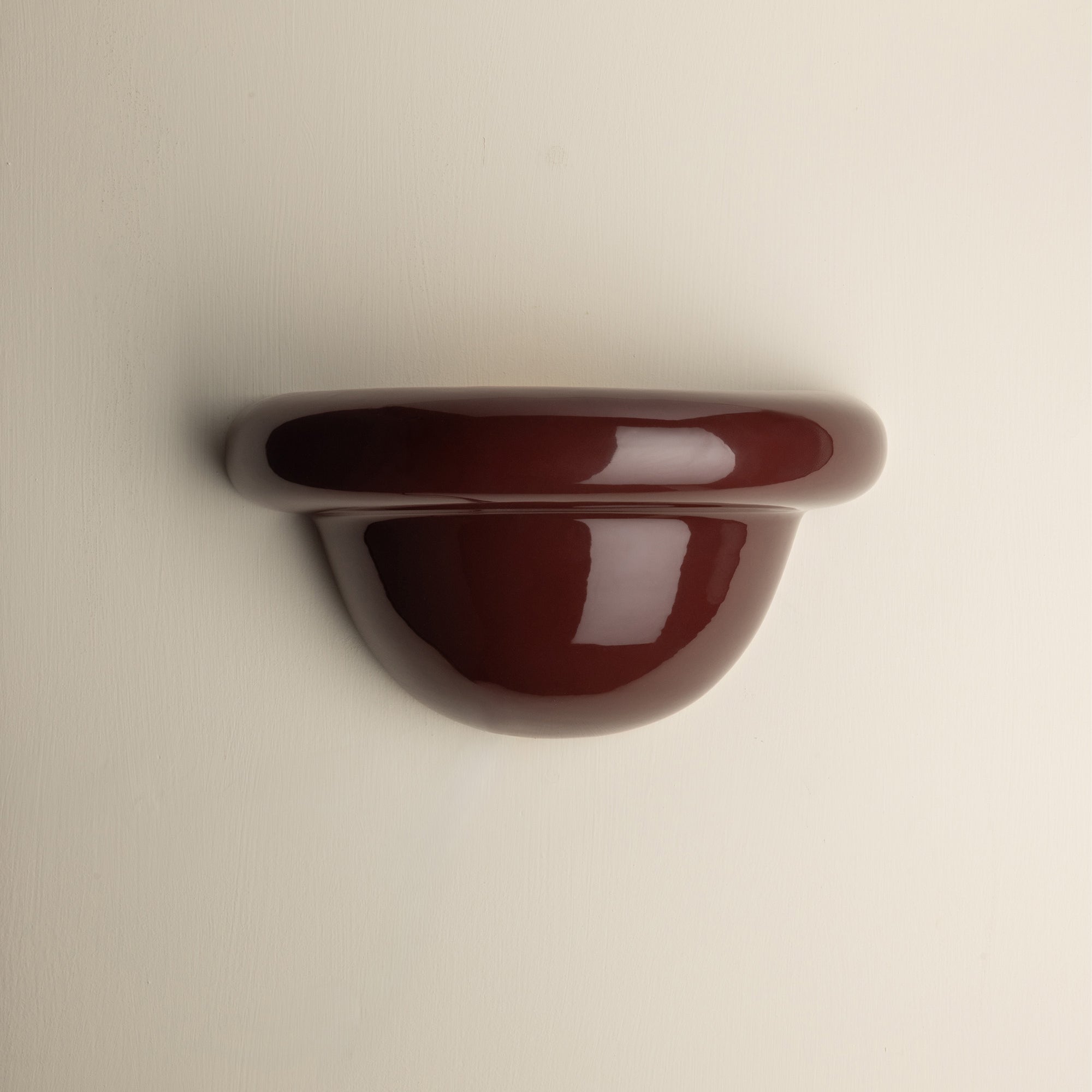 A glossy, dark reddish-brown wall-mounted shelf or hook with a rounded, semi-circular profile, shown against a plain off-white background.