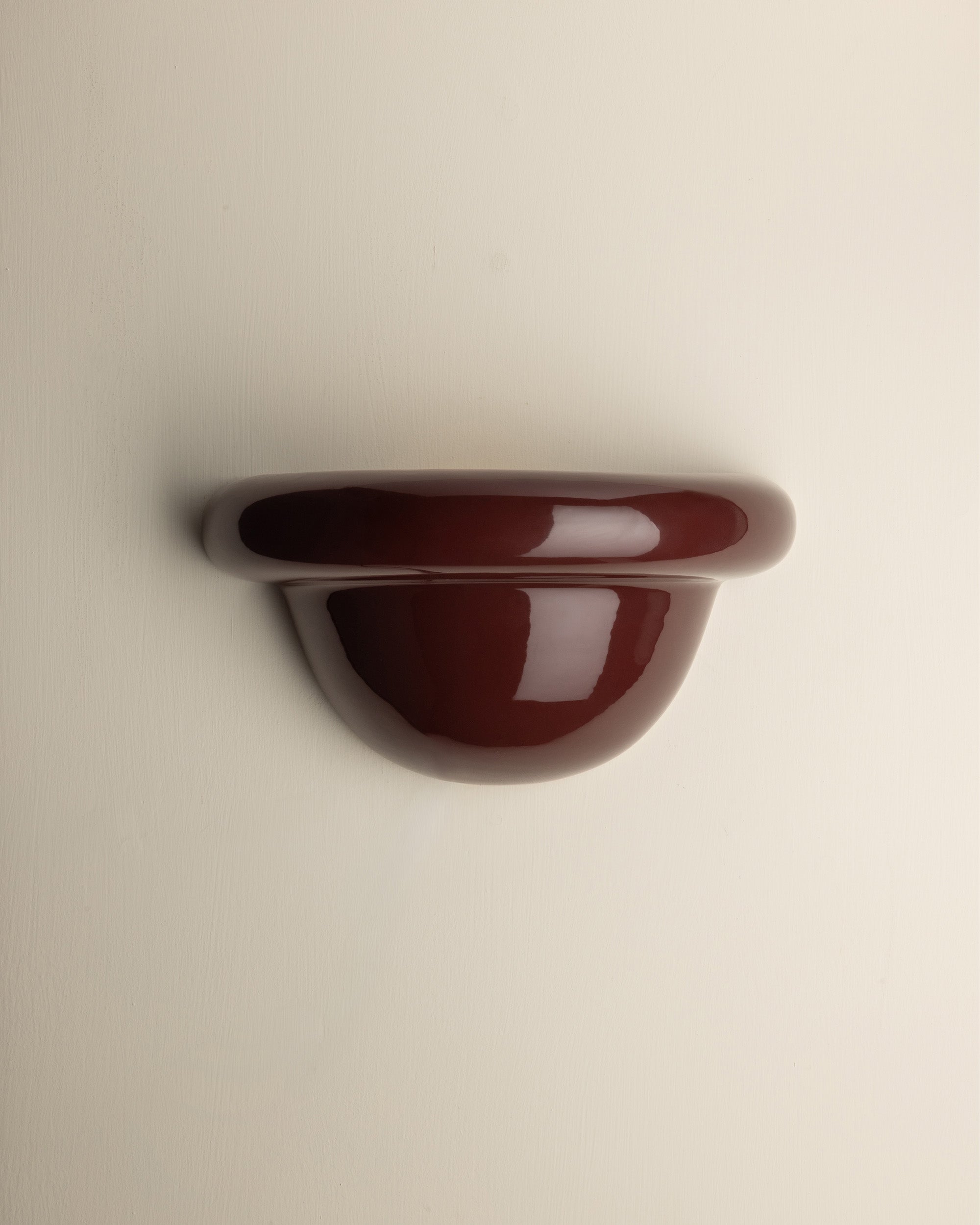 A glossy, dark reddish-brown wall-mounted shelf or hook with a rounded, semi-circular profile, shown against a plain off-white background.