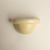A glossy, dome-shaped wall-mounted sconce in a pale cream or butter yellow color, shown against a plain, light beige wall.