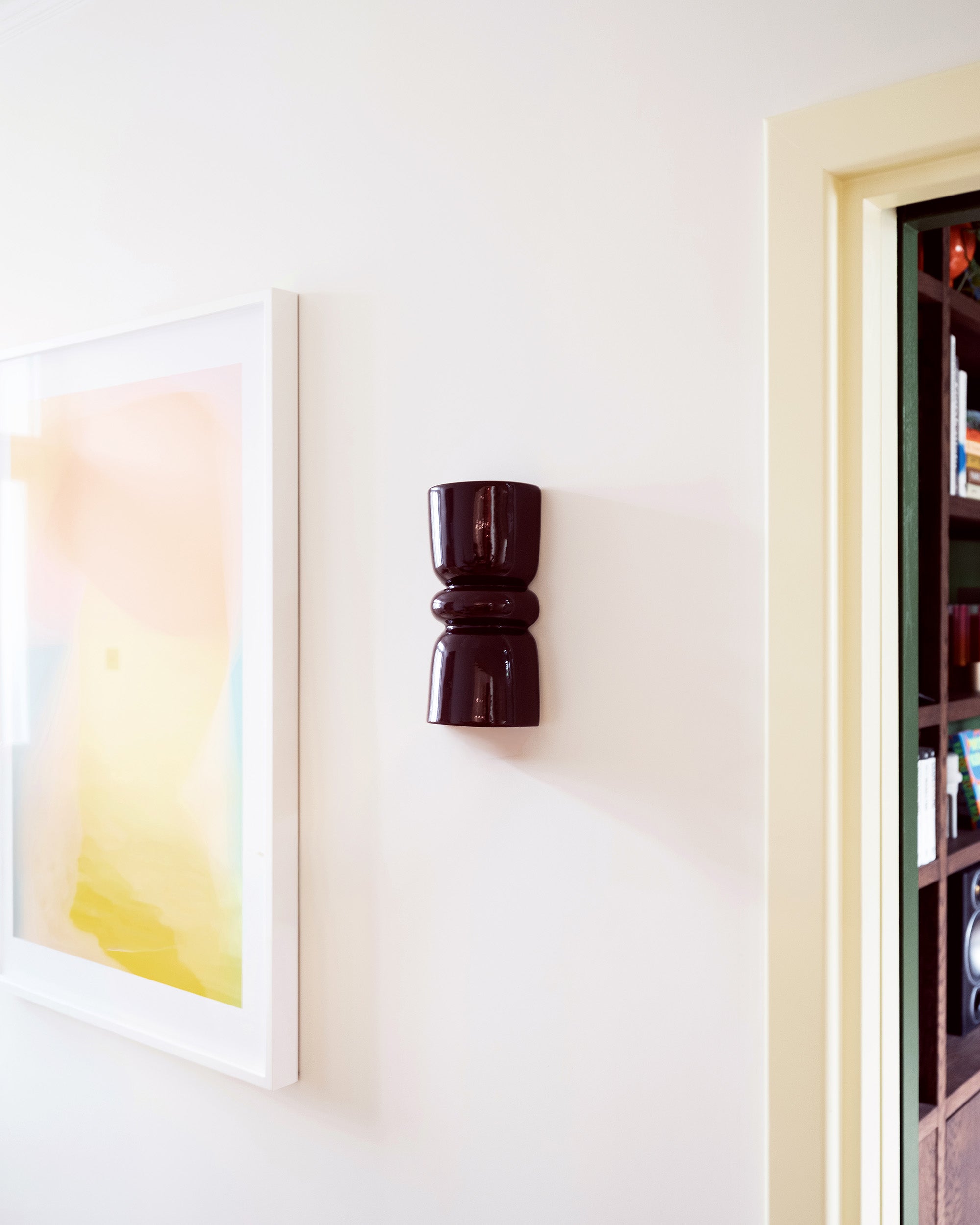 Late Afternoon Lighting Burgundy Up and Down lighter Ceramic Wall Sconce on a white wall with a piece of art.