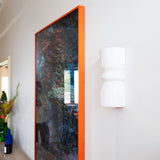 Late Afternoon Lighting White Up and Down lighter Ceramic Wall Light on a white wall next to a photograph in a red frame