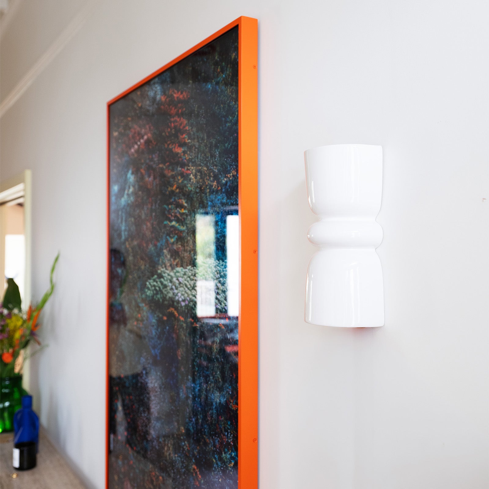 Late Afternoon Lighting White Up and Down lighter Ceramic Wall Light on a white wall next to a photograph in a red frame