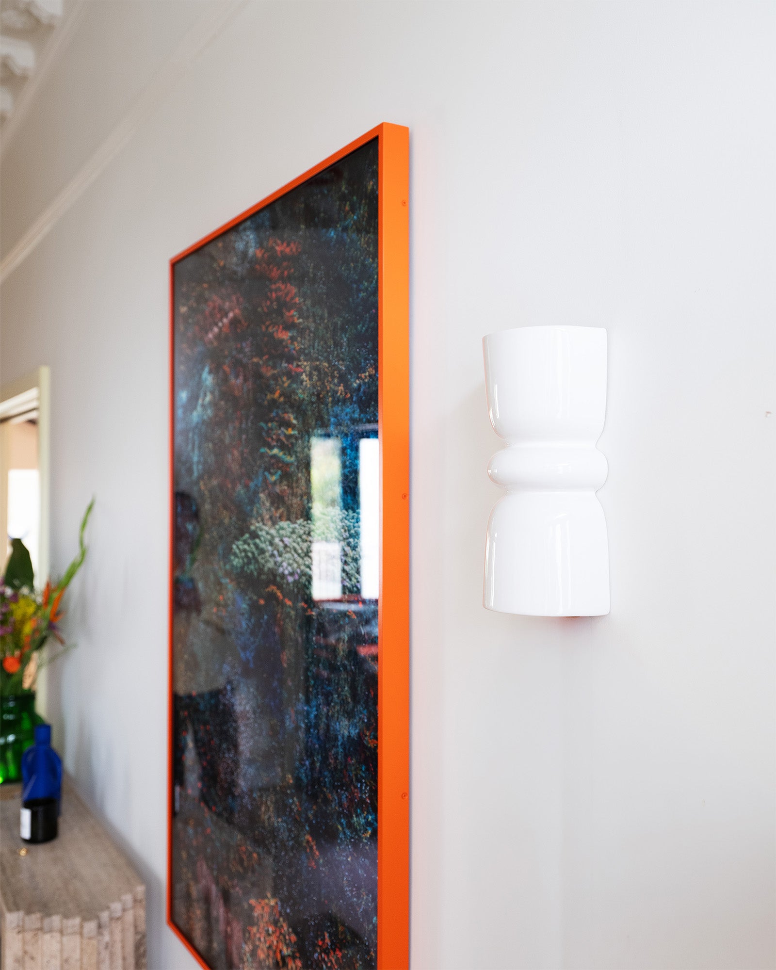 Late Afternoon Lighting White Up and Down lighter Ceramic Wall Light on a white wall next to a photograph in a red frame