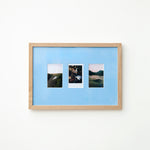 A light wood framed wall art piece with a Sky blue mount and three small vertical landscape photographs arranged side by side, mounted on a plain white wall.