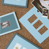A styled flat-lay of light blue picture frames and matching mat boards arranged on a brown woven rug, with a few sample photographs placed on top.