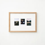 A light natural wood frame with a white mat holding three small landscape photographs, displayed against a plain white wall.