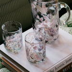 Clear glass pitcher and tumblers with floral design on a book