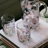Clear glass pitcher and tumblers with floral design on a book