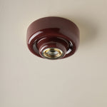 A glossy dark burgundy glass ceiling light fixture with a brass screw base, mounted on a textured off-white ceiling.