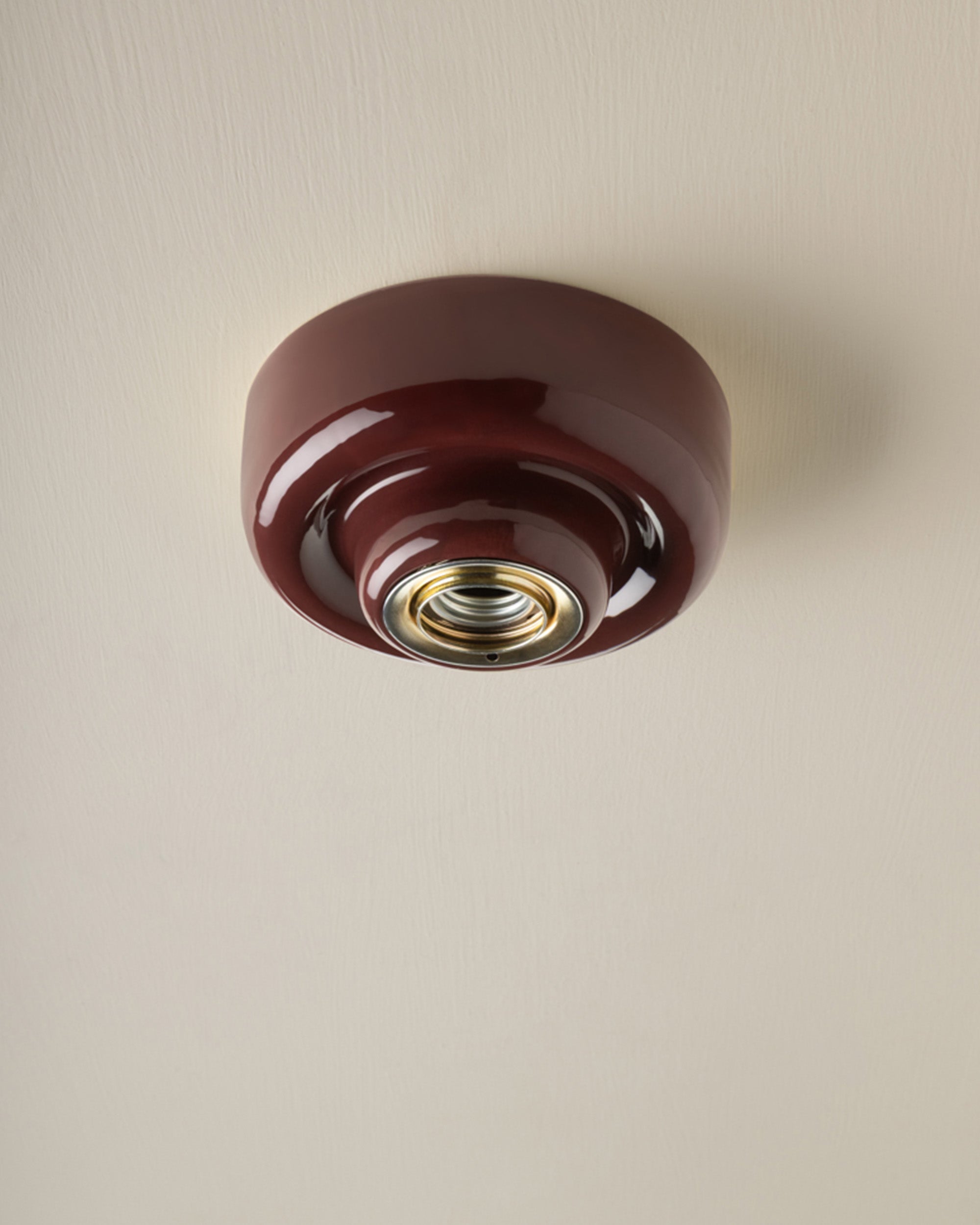 A glossy dark burgundy glass ceiling light fixture with a brass screw base, mounted on a textured off-white ceiling.