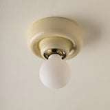 A classic ceiling-mounted light fixture with a round butter yellow-coloured ceramic or plaster canopy and a frosted white globe bulb, shown against a matching textured off-white ceiling.