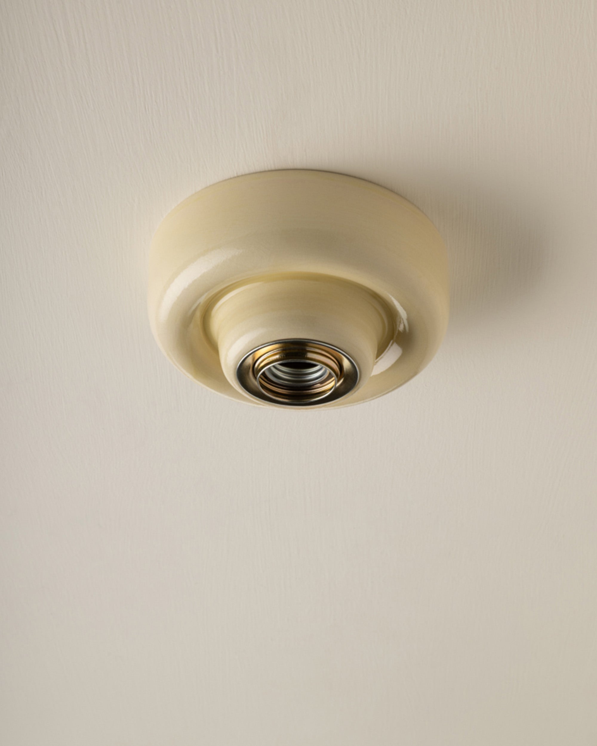 A vintage-style butter yellow-coloured ceiling light fixture with a circular ceramic shade and a brass screw base, shown mounted on a textured off-white ceiling.