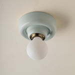 A ceramic ceiling-mounted light fixture in pale blue-green and a frosted white globe bulb, shown against a warm off-white ceiling.