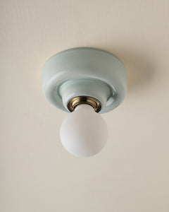 A ceramic ceiling-mounted light fixture in pale blue-green and a frosted white globe bulb, shown against a warm off-white ceiling.
