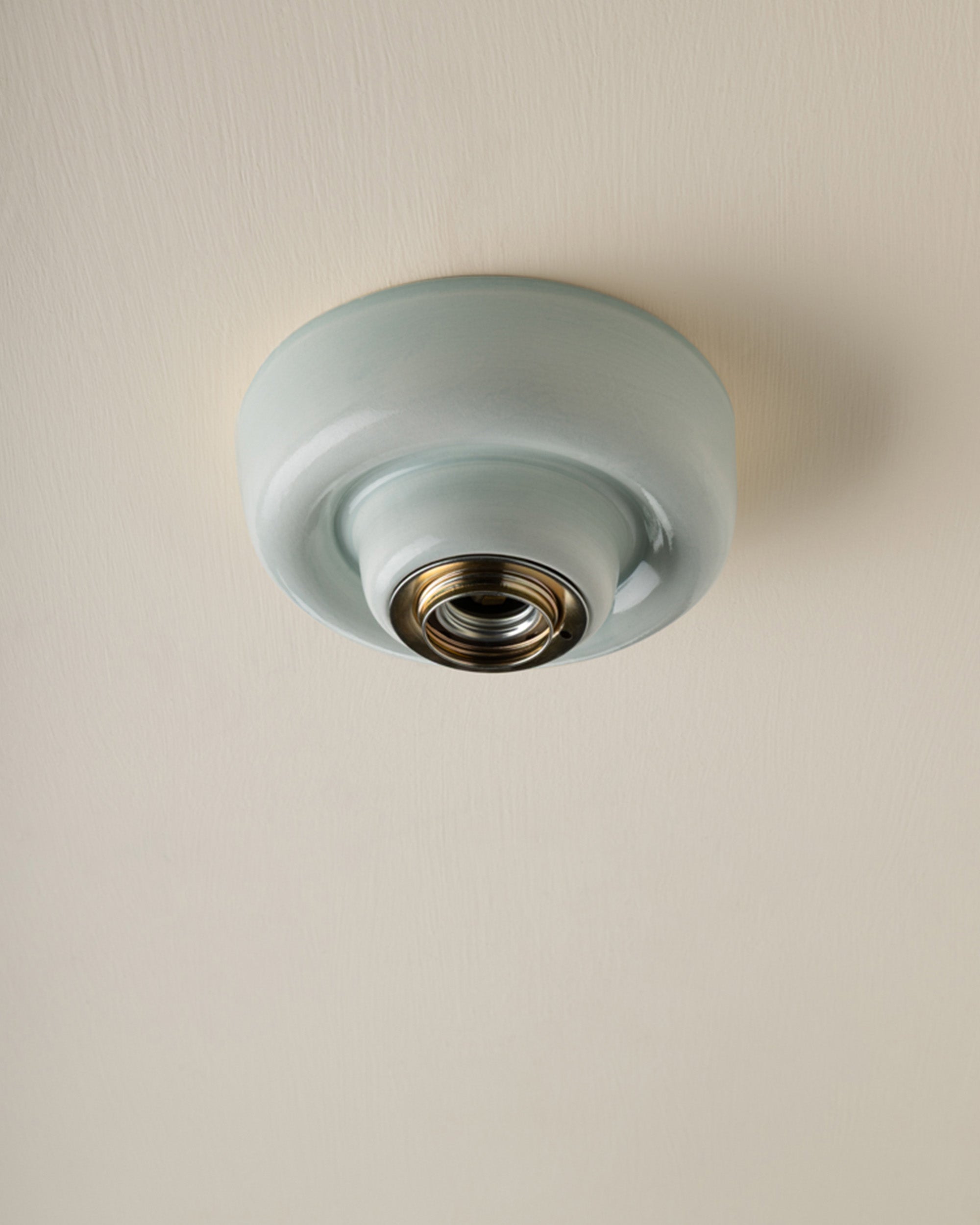 A round, semi-glossy pale blue green ceiling light fixture with a brass socket, shown mounted on a textured off-white ceiling.