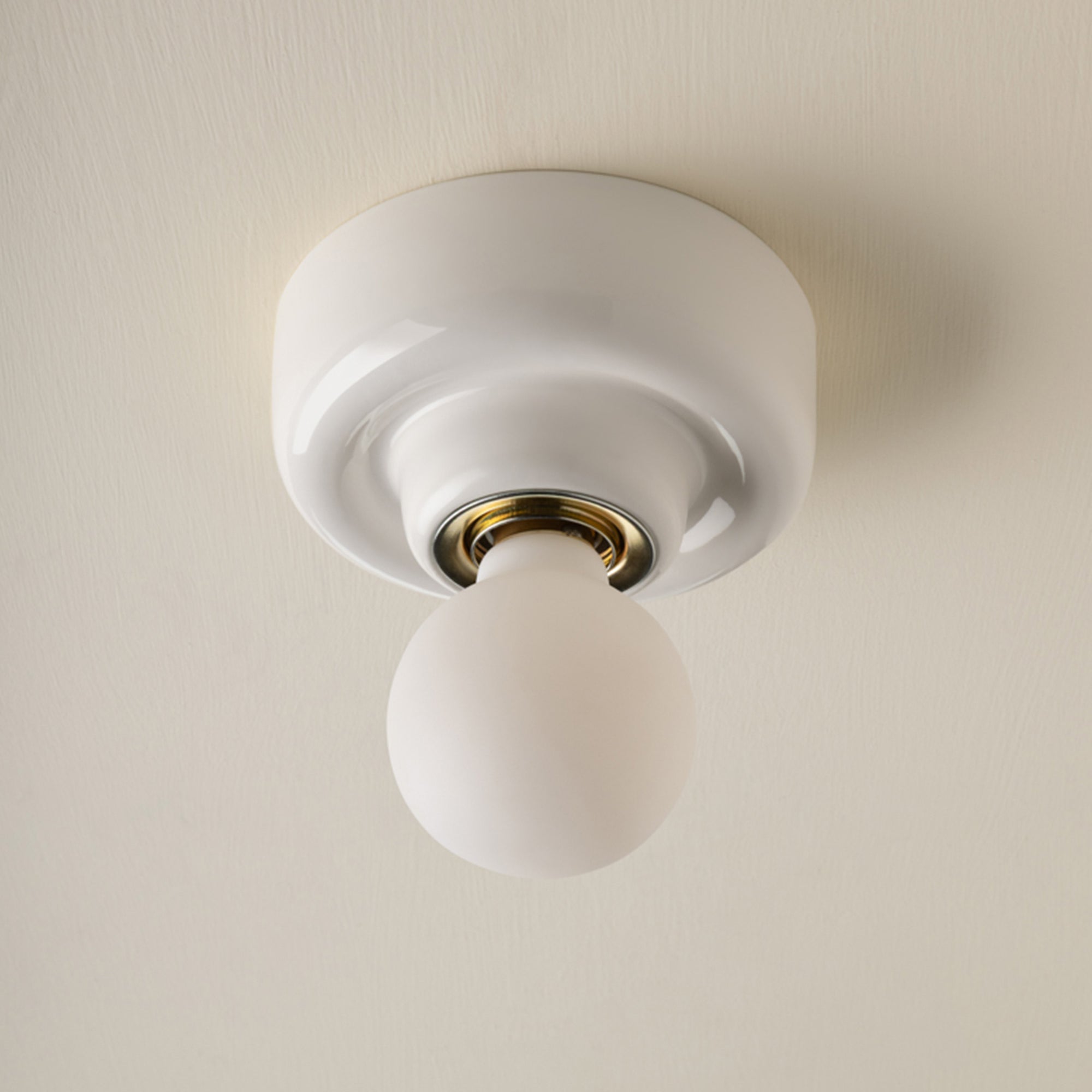 A modern minimalist ceiling light fixture with a white circular canopy and a frosted glass globe bulb, set against a warm off-white textured ceiling.