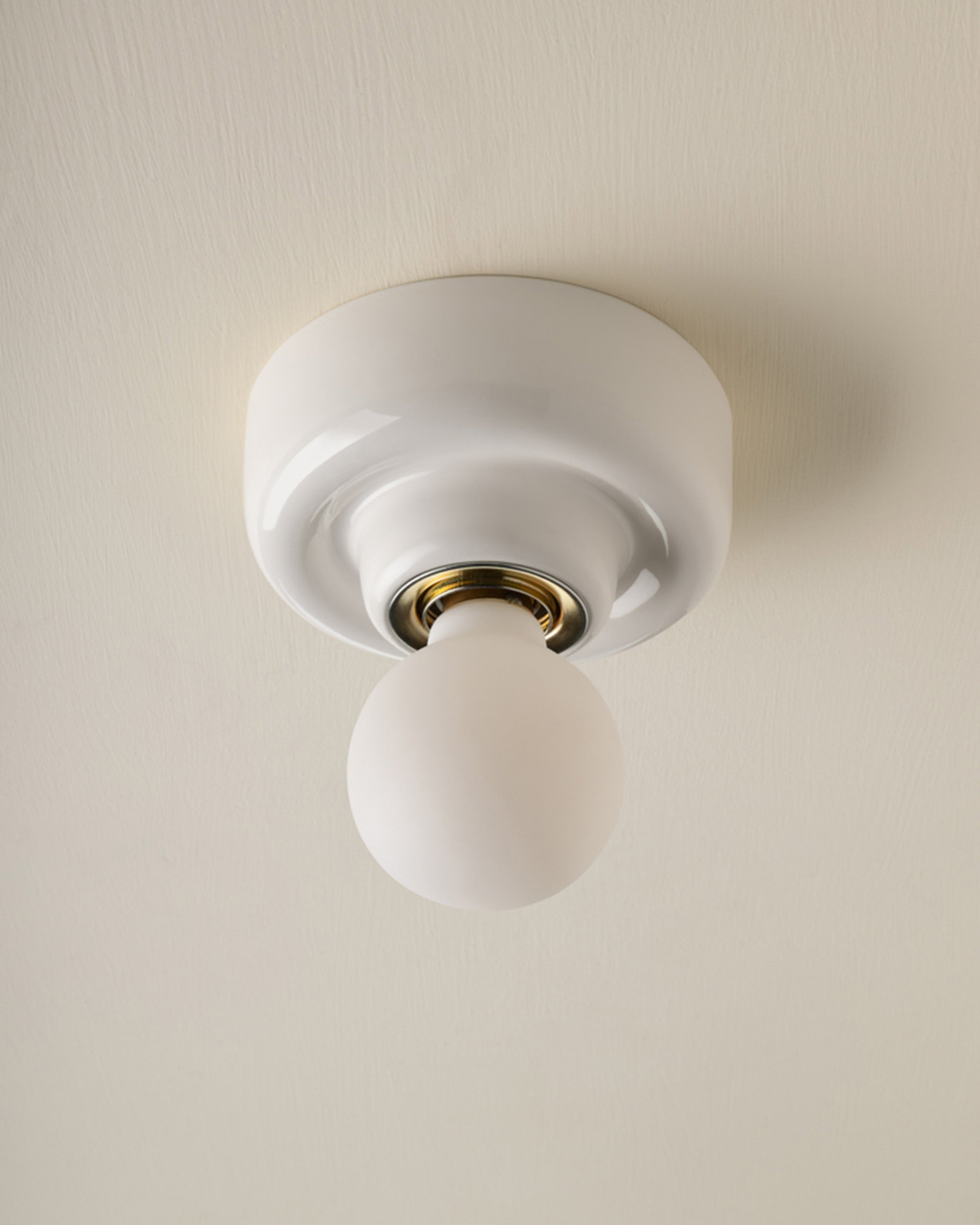 A modern minimalist ceiling light fixture with a white circular canopy and a frosted glass globe bulb, set against a warm off-white textured ceiling.