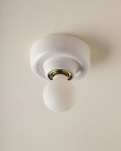 A modern minimalist ceiling light fixture with a white circular canopy and a frosted glass globe bulb, set against a warm off-white textured ceiling.
