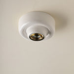 A white ceramic flush-mount ceiling light fixture with a gold-toned metal socket, shown installed on a textured off-white ceiling.