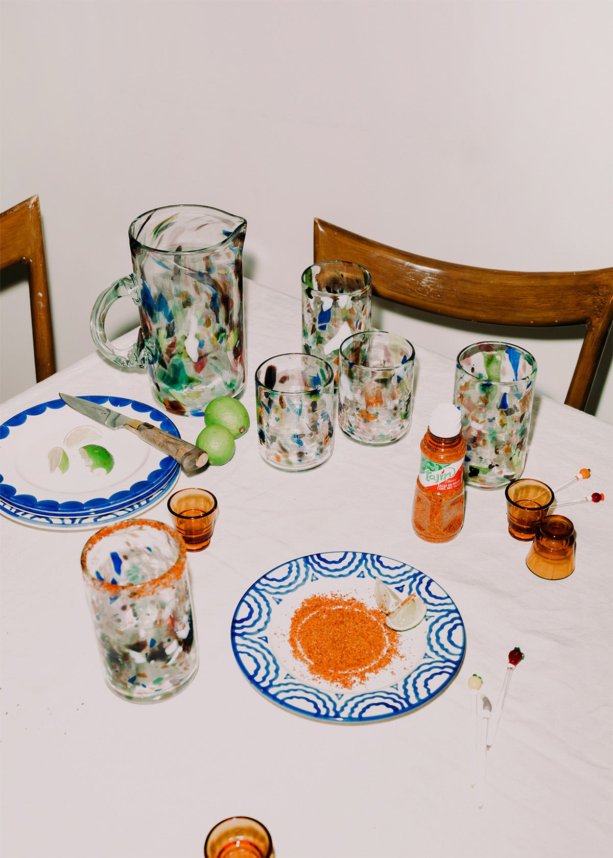 Cocktsil table with colorful glassware, plates, and a knife on a white tablecloth.